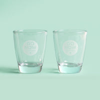 Twee lege Go Now shotglazen met gegraveerd logo op een mintgroene achtergrond