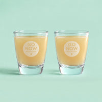 Twee Go Now shotglazen gevuld met gembersap op een mintgroene achtergrond